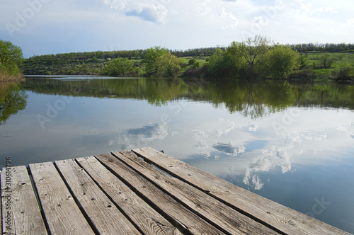 Wooden pier on a river. Cloudy sky reflected in water. Warm sunny day. Traditional nature landscape in central Ukraine.