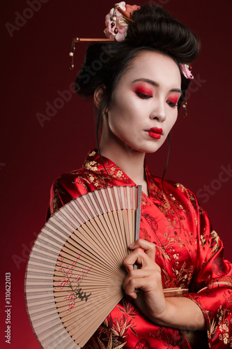 Image of young geisha woman in japanese kimono holding wooden hand fan