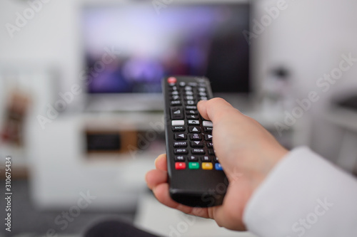 Watching TV and using remote controller. Hand with remote controller changing channels or opening apps on smart tv