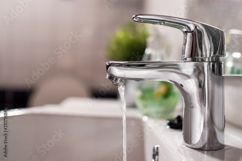 Cold water flowing from faucet in clean bright bathroom