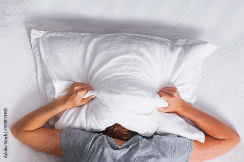Woman lying on the bed and covering her head with pillow.