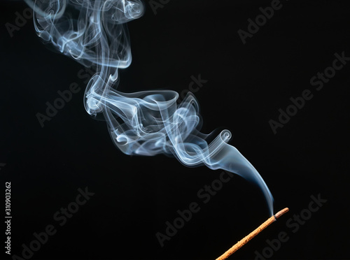 Burning incense stick with smoke on black background.