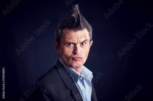 Man with mohawk wearing suit in front of black background.
