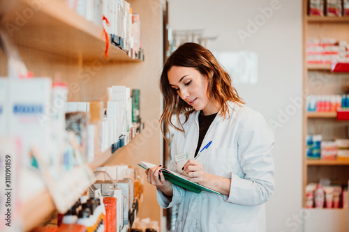 .Young female pharmacist working in her large pharmacy. Placing medications, taking inventory. Lifestyle