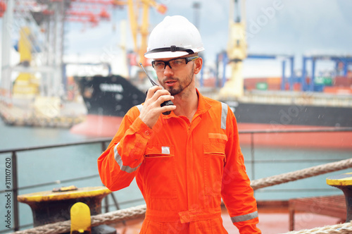 An experienced sailor in orange overalls and a white helmet works on a bulk carrier.