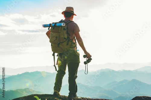 The hiker with a backpack stood on the rock after examining the map to find a path in a beautiful mountain landscape.