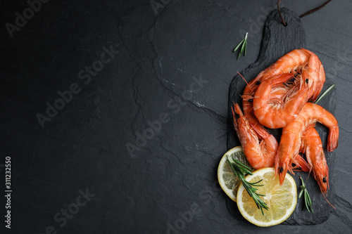 Delicious cooked shrimps with lemon and rosemary on black table, flat lay. Space for text