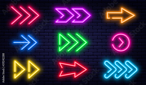 Set of glowing neon arrows. Glowing neon arrow pointers on brick wall background. Retro signboard with bright neon tubes in red, yellow, purple and blue colors