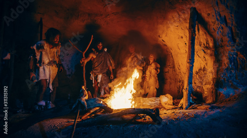 Tribe of Prehistoric Hunter-Gatherers Wearing Animal Skins Stand Around Bonfire Outside of Cave at Night. Portrait of Neanderthal / Homo Sapiens Family Doing Pagan Religion Ritual Near Fire