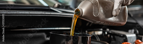 partial view of mechanic pouring machine oil at car engine, panoramic shot