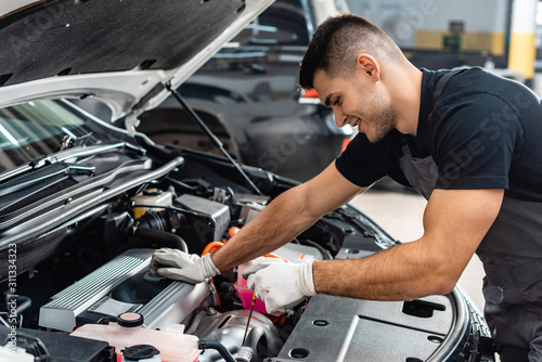 smiling mechanic checking engine oil level with dipstick