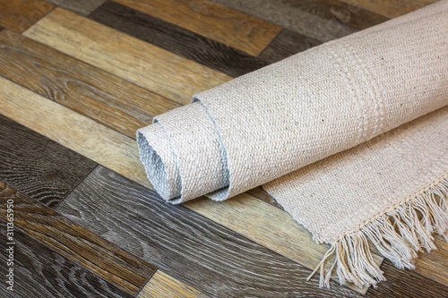 Rolled natural cotton rug on the wooden linoleum background.