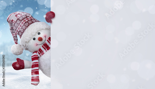 Happy snowman in the winter scenery behind the blank advertising banner with copy space