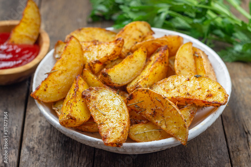 Baked potato with spices, herbs and ketchup in a plate on the wooden table.