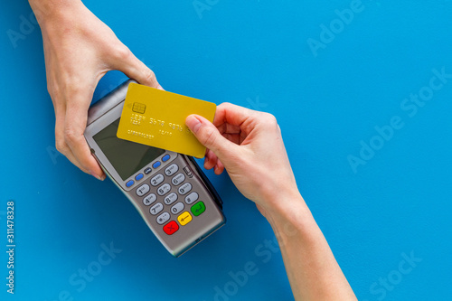 Contactless payment, paypass. Hand hold bank card near terminal on blue background top-down copy space