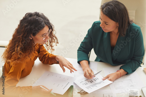 Two young businesswomen working on new business plan sitting together at office desk, high angle horizontal shot