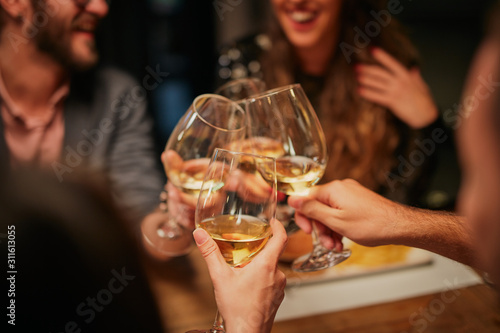 Best friends sitting in restaurant for dinner and making a toast with white wine. On table is food.