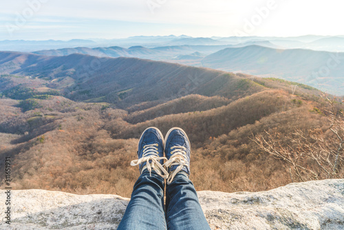 Woman's feet in blue sneakers on the edge of a high cliff