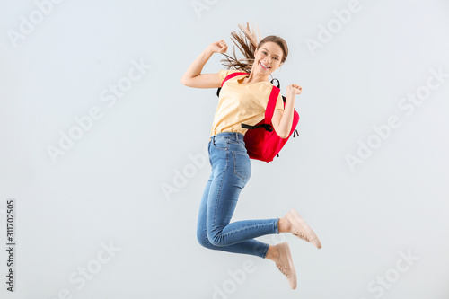 Jumping female student against light background