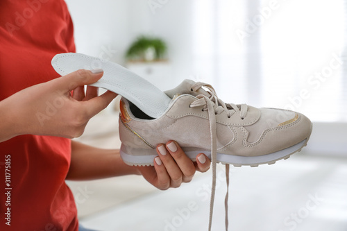 Woman putting orthopedic insole into shoe at home, closeup