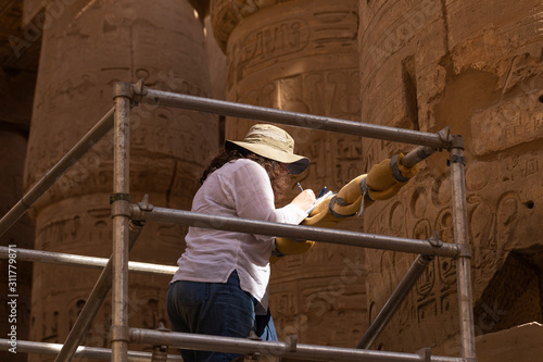 Karnak Temple, complex of Amun-Re. Embossed hieroglyphics on columns. Great Hypostyle Hall. A French historian studies columns damaged by French vandal -soldiers during the colonization of Egypt.