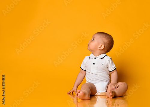 Infant baby boy toddler is sitting on the floor looking up at free copy space in corner yellow background