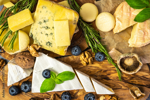Different types of cheese with herbs, blueberries, walnut, dried mushrooms on a wooden board