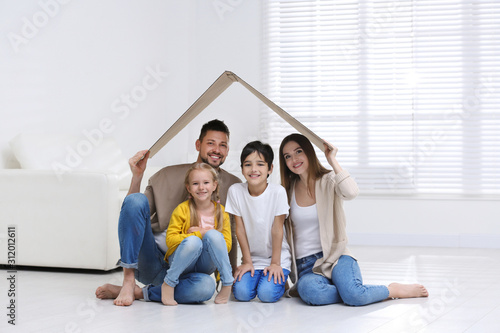 Happy family sitting under cardboard roof at home. Insurance concept