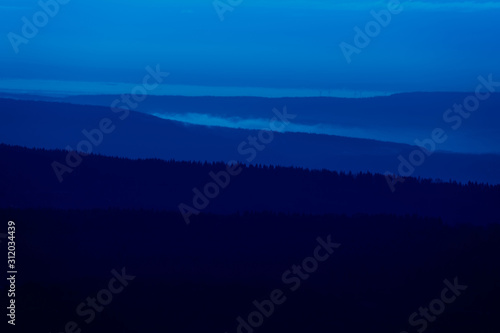Blue evening hilly landscape at the edge of a German low mountain range with fir forests, blue hour