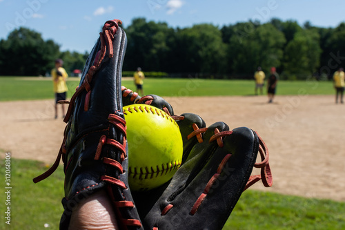 a man holds a freshly caught green softball in a black baseball glove during a softball tournament game with teammates in the background
