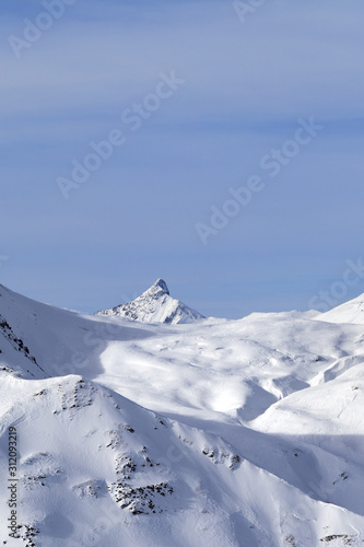 Snowy off-piste slope, sunlit plateau and peak at high winter mountains