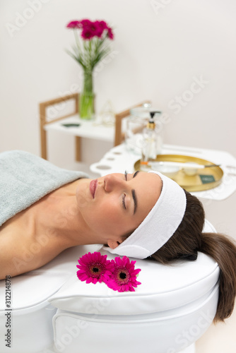 Zrelaksowana kobieta w salonie kosmetycznym podczas masażu twarzy. Kobieta leżąca na fotelu w salonie masażu kobido. 