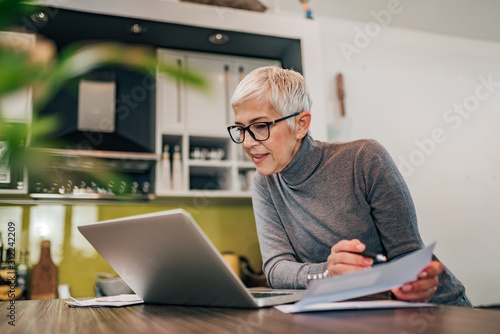 Charming woman holding papers and looking at laptop, portrait.