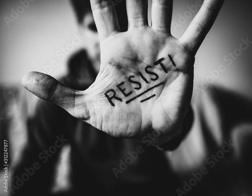 Man holds hand to camera with RESIST written on palm.