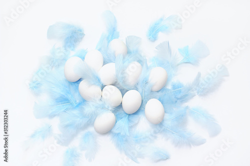 Creative layout for Easter. eggs of white color surrounded by blue feathers on a light background. top view, flat lay