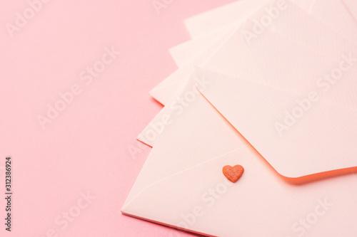 Pink envelopes arranged in fan with one small red candy heart on top on monochrome pastel background. Valentine love letters charity donation mother's day concept