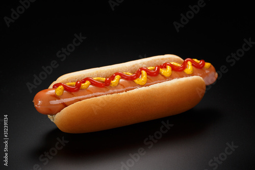 Classic hot dog with ketchup and mustard on a black background.