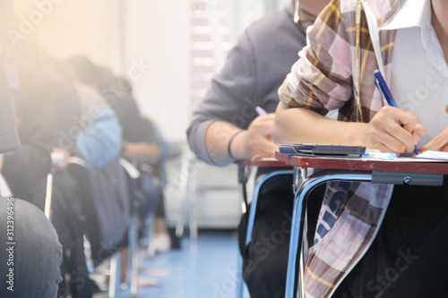 Hands university student holding pen writing /calculator doing examination / study or quiz, test from teacher or in large lecture room, students in uniform attending exam classroom educational school.