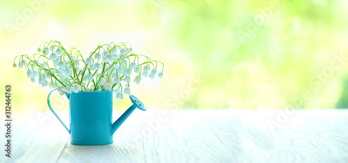 Lily of the valley in watering can on white table. symbol of spring season holiday, flowering spring time, inspiring mood. beautiful romantic composition. banner. copy space