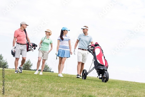 Friends talking while walking at golf course against clear sky