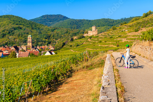 Young woman cycling on road along vineyards from Riquewihr to Kaysersberg village, Alsace Wine Route, France