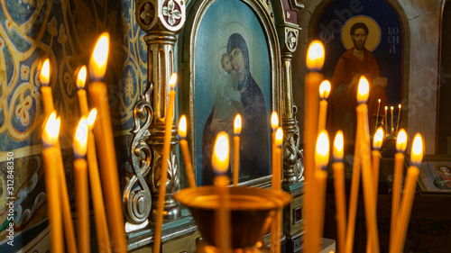 Blurred wax burning candles in an orthodox church on the icon background.