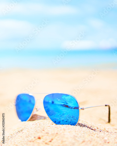 Blue sunglasses on the beach sand with blue sky on background