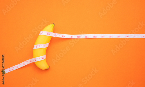 Yellow banana with measurement tape on orange background. Men penis size concept with empty free space for text or design