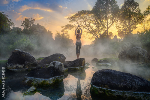 young woman in action of yoga practice in steaming hot spring water, the nature yoga exercise in hot spring steaming water at morning sunrise