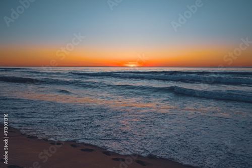 Abstract seascape. Beautiful tropical beach at sunset. Blue ocean, colorful sky, and sun setting down the horizon