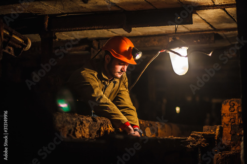 A tired miner in a coal mine looks at the light. Work in a coal mine. Portrait of a miner. Copy space.