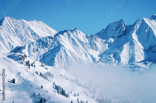 Landscape in Zillertal Arena ski resort in clouds in Tyrol at Mayrhofen in Austria in winter Alps. Alpine mountains with white snow and blue sky. Downhill peaks at Austrian snowy slopes.