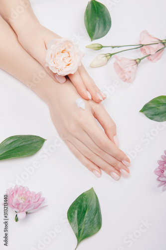 Top view cosmetic cream on female hands with pink flowers on white background, flat lay. Concept spa skin care