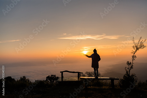 Silhouette lonely girl standing on top of mountain with sunrise.Tourist traveler at sunrise.